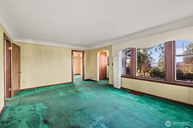 carpeted empty room featuring baseboards and arched walkways