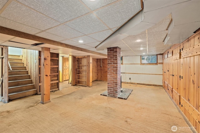 basement with a paneled ceiling, wooden walls, stairs, and carpet