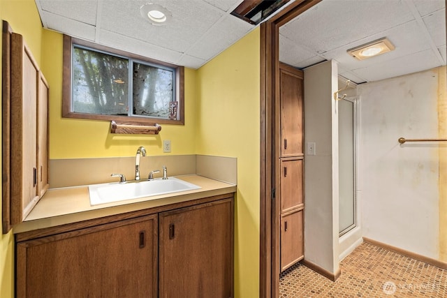 bathroom featuring vanity, a paneled ceiling, a stall shower, and baseboards