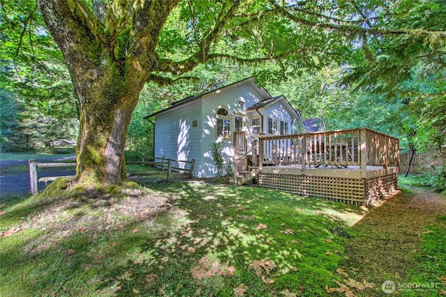 rear view of house with a yard, a wooden deck, and fence