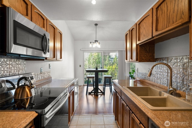 kitchen featuring light tile patterned floors, stainless steel appliances, a sink, brown cabinetry, and decorative light fixtures