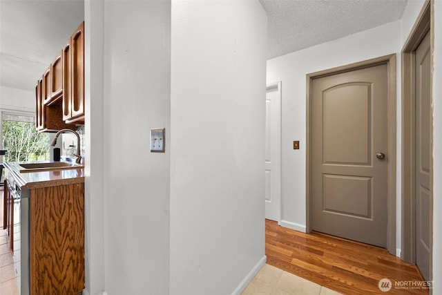 corridor with a textured ceiling, a sink, light wood-style flooring, and baseboards