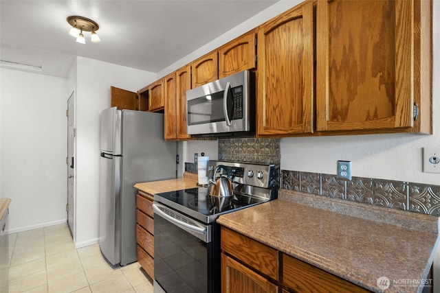 kitchen featuring light tile patterned floors, baseboards, appliances with stainless steel finishes, brown cabinets, and tasteful backsplash