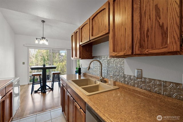 kitchen featuring a notable chandelier, a sink, backsplash, brown cabinetry, and pendant lighting