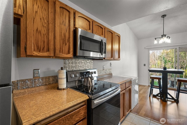 kitchen featuring appliances with stainless steel finishes, a chandelier, brown cabinetry, and light tile patterned floors