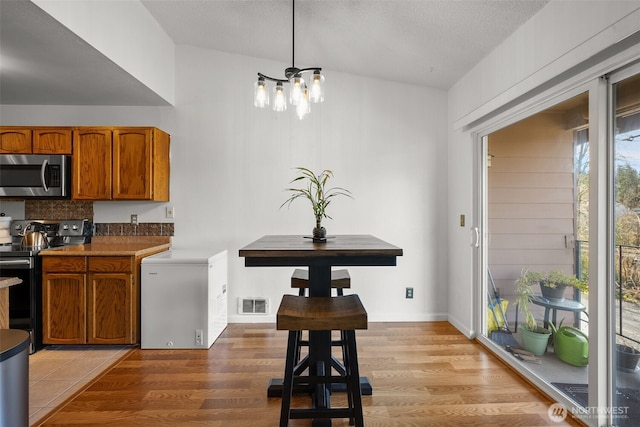 kitchen featuring light wood finished floors, stainless steel microwave, brown cabinets, black range with electric stovetop, and refrigerator