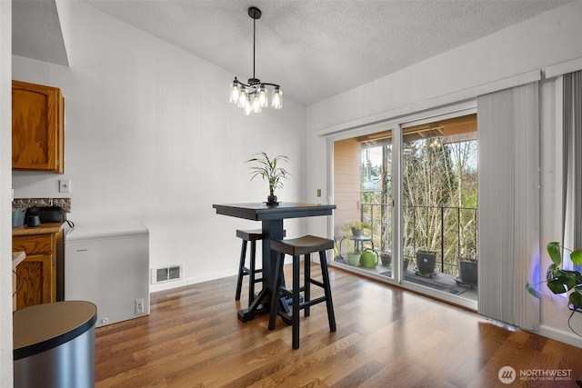 dining space with dark wood-style floors, visible vents, vaulted ceiling, and a notable chandelier