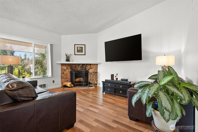 living room with a textured ceiling, visible vents, wood finished floors, and a stone fireplace