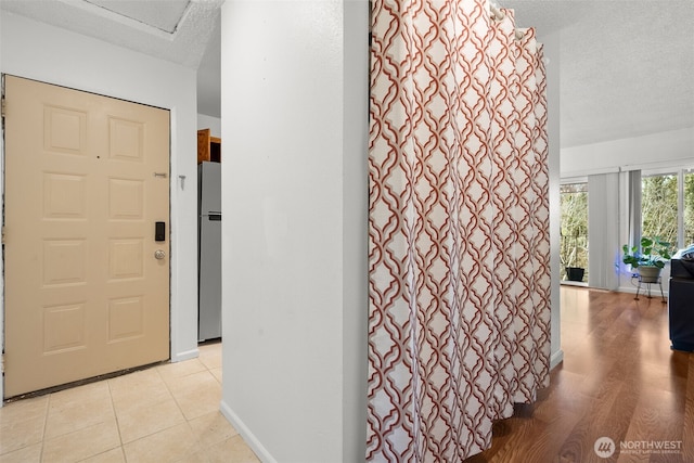 hall with a textured ceiling, baseboards, and light tile patterned floors