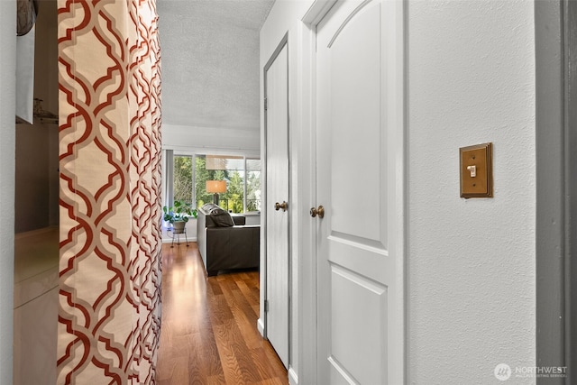 corridor with a textured wall, a textured ceiling, and wood finished floors