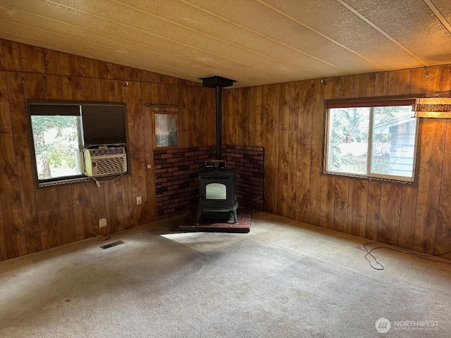 unfurnished living room with a wood stove, a wealth of natural light, carpet, and visible vents