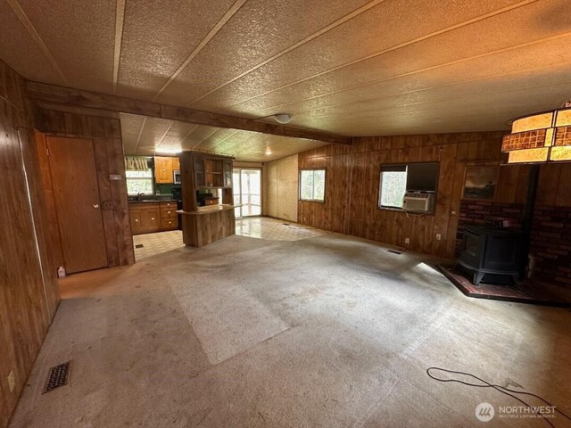 unfurnished living room featuring plenty of natural light, a wood stove, light carpet, and wood walls