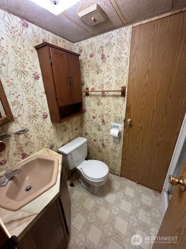 half bathroom featuring toilet, wallpapered walls, vanity, and tile patterned floors