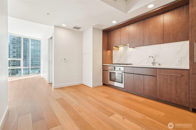 kitchen featuring oven, a sink, backsplash, gas stovetop, and light wood-style floors