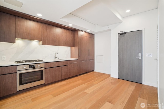 kitchen featuring light wood finished floors, a sink, backsplash, appliances with stainless steel finishes, and light countertops