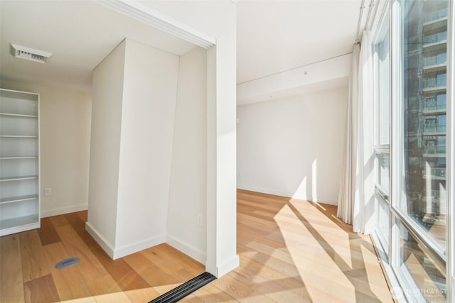 hall with visible vents, baseboards, and light wood-style floors