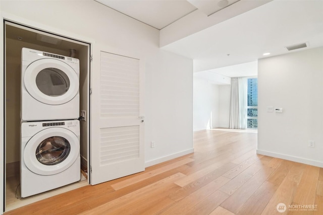 laundry area with visible vents, light wood finished floors, stacked washer / drying machine, baseboards, and laundry area