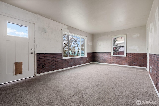 foyer with a wainscoted wall, brick wall, and carpet flooring