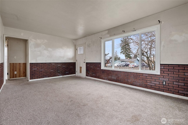 carpeted empty room with a wainscoted wall and brick wall