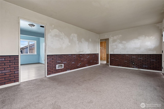 carpeted empty room featuring a wainscoted wall and brick wall