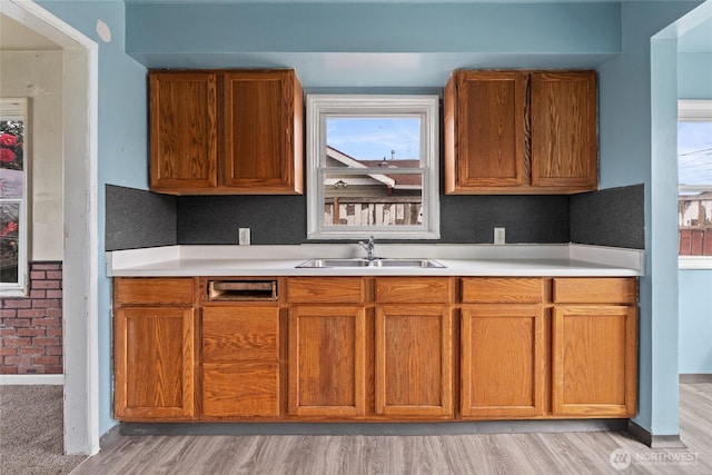 kitchen with light wood finished floors, brown cabinets, a sink, and light countertops