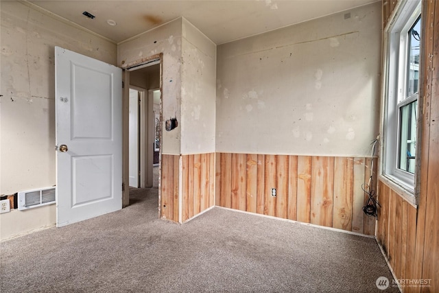 carpeted spare room featuring a wainscoted wall, visible vents, and wooden walls