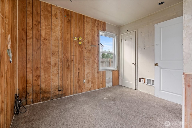 carpeted empty room with wood walls and visible vents