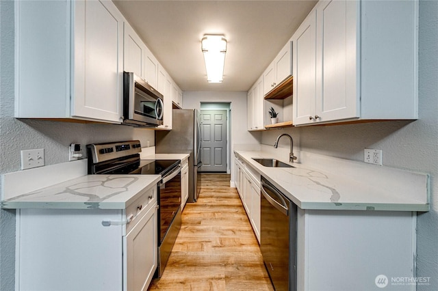 kitchen with light wood finished floors, stainless steel appliances, white cabinetry, a sink, and light stone countertops