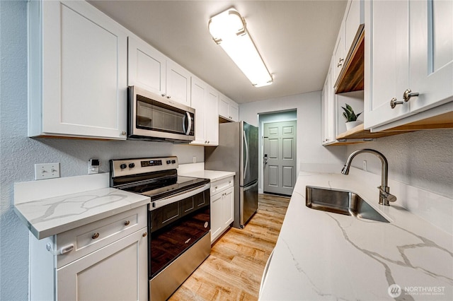 kitchen featuring stainless steel appliances, a sink, white cabinetry, light stone countertops, and light wood finished floors