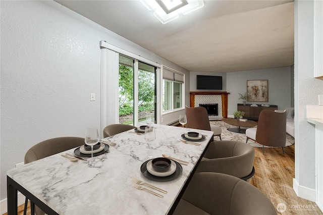 dining room with light wood-style flooring, a fireplace, and a textured wall