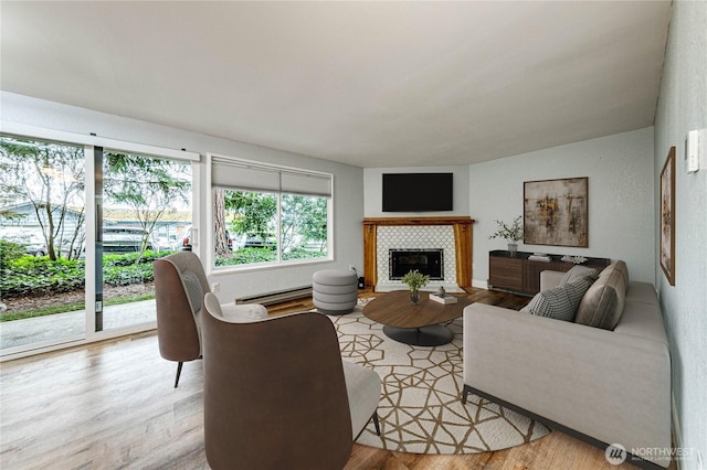 living room with a tiled fireplace, a baseboard radiator, and light wood-style floors