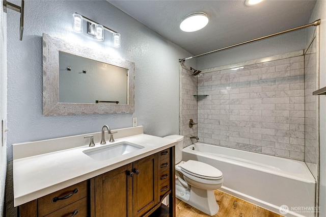 full bath with a textured wall, toilet, wood finished floors, vanity, and washtub / shower combination