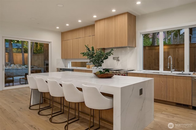 kitchen with tasteful backsplash, light wood-style flooring, modern cabinets, a kitchen island, and a sink