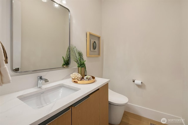 bathroom with wood finished floors, vanity, toilet, and baseboards