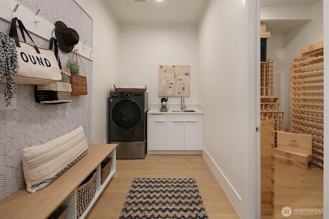 clothes washing area featuring light wood finished floors, washer / clothes dryer, cabinet space, a sink, and baseboards