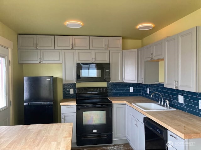 kitchen featuring decorative backsplash, butcher block counters, black appliances, and a sink