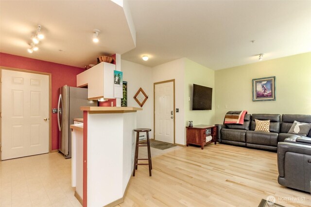 kitchen featuring light wood-style flooring, a peninsula, open floor plan, freestanding refrigerator, and a kitchen bar