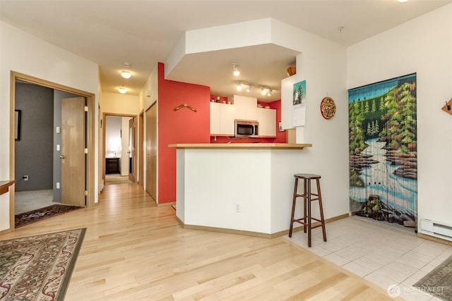 kitchen with a breakfast bar area, stainless steel microwave, light wood-style floors, white cabinetry, and baseboards