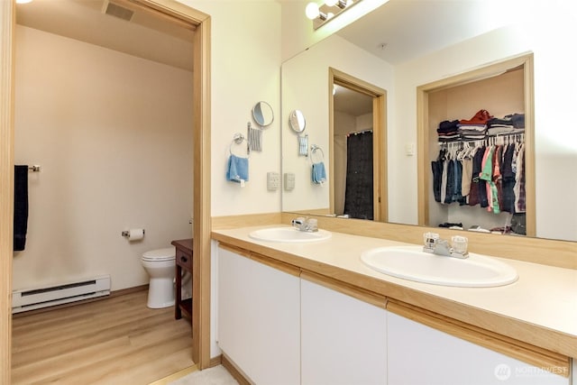 bathroom with toilet, visible vents, a baseboard heating unit, and a sink