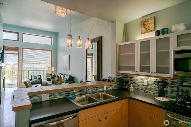 kitchen featuring appliances with stainless steel finishes, open floor plan, a peninsula, a sink, and backsplash