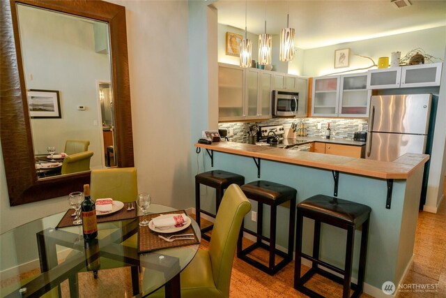 kitchen featuring a notable chandelier, stainless steel appliances, a peninsula, a kitchen breakfast bar, and backsplash