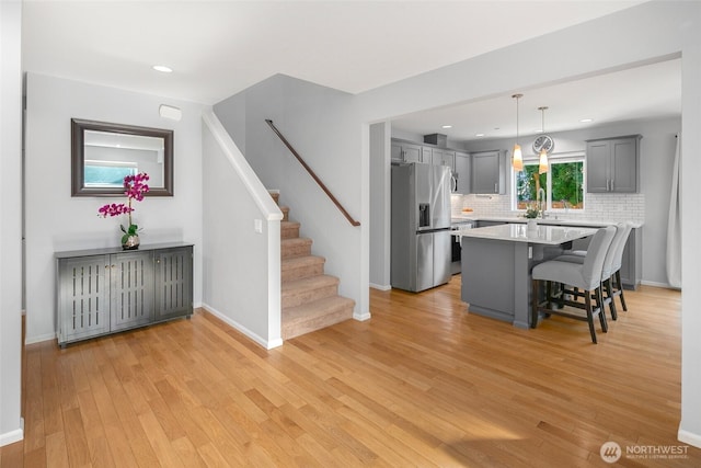 kitchen with stainless steel fridge with ice dispenser, a breakfast bar, light countertops, gray cabinets, and light wood-style floors