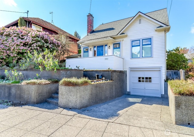 view of front of house featuring an attached garage, roof with shingles, concrete driveway, and a chimney