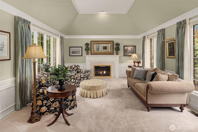 carpeted living room featuring visible vents, lofted ceiling, a glass covered fireplace, wainscoting, and a decorative wall