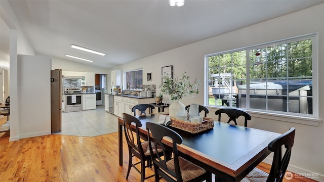 dining space with light wood-style floors and vaulted ceiling