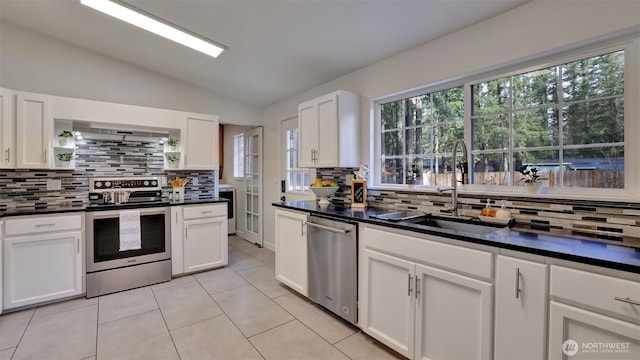 kitchen featuring dark countertops, lofted ceiling, white cabinets, stainless steel appliances, and a sink