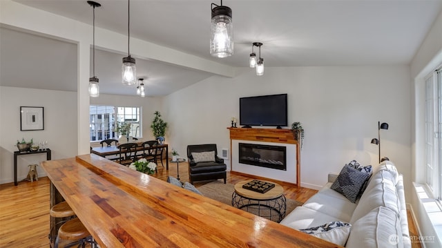 living area featuring a glass covered fireplace, light wood-style flooring, vaulted ceiling with beams, and baseboards