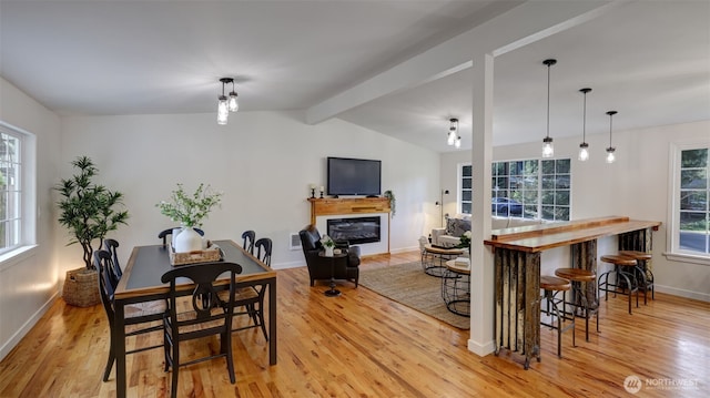 dining space with a glass covered fireplace, lofted ceiling with beams, plenty of natural light, and light wood-style floors