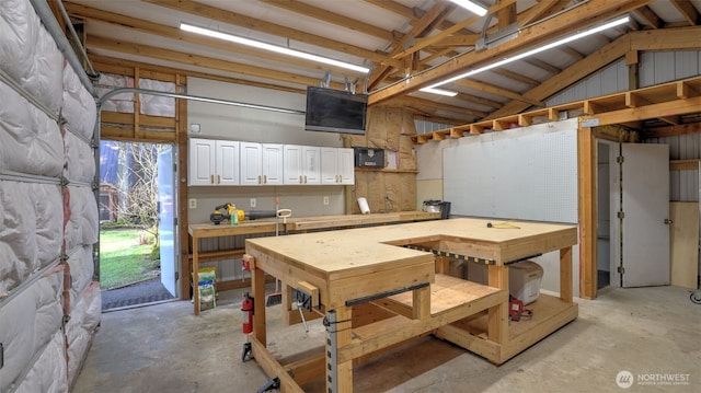 interior space featuring a garage, lofted ceiling, a workshop area, and unfinished concrete flooring