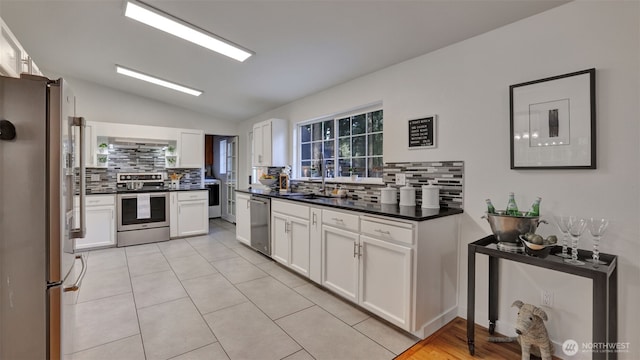 kitchen featuring lofted ceiling, stainless steel appliances, white cabinetry, dark countertops, and tasteful backsplash